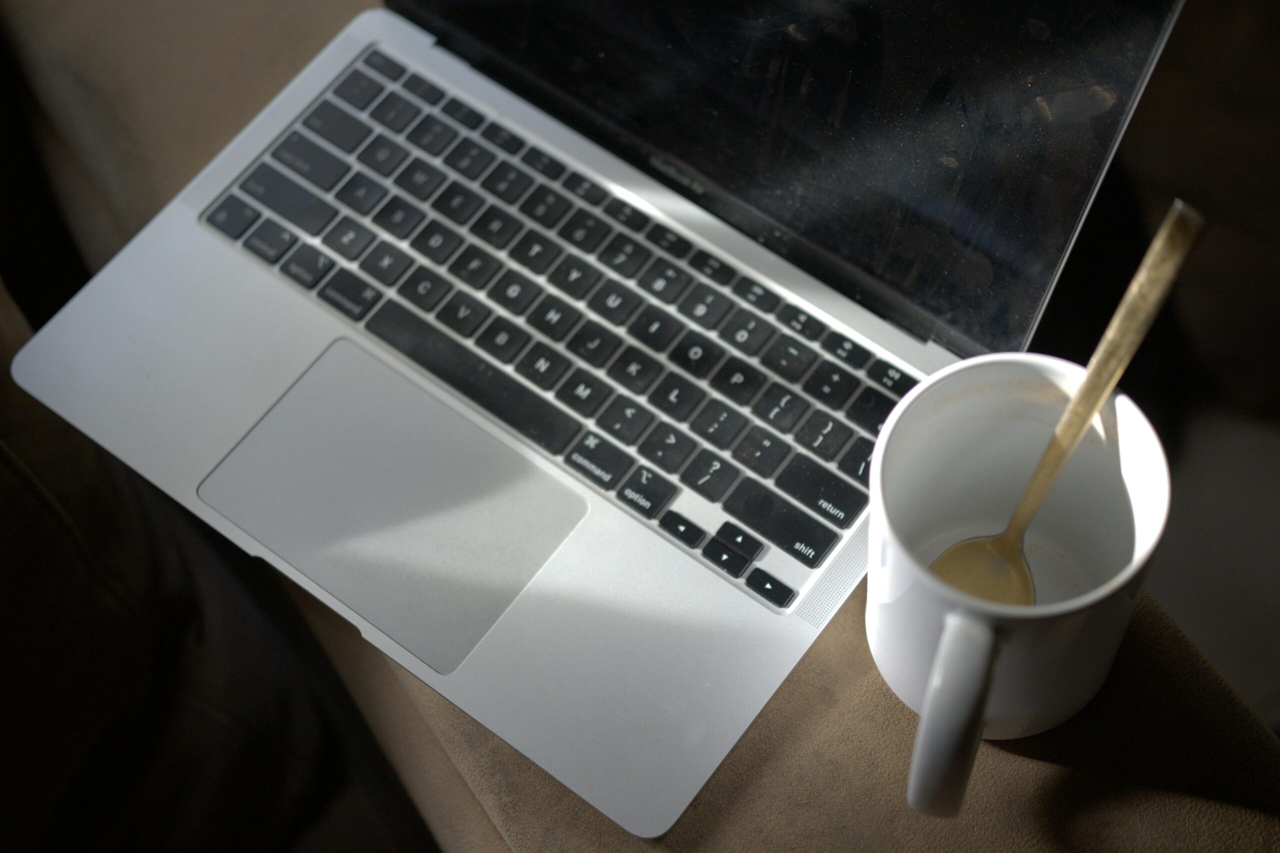 A laptop and empty coffee mug with a spoon on a couch, capturing a work-from-home vibe.