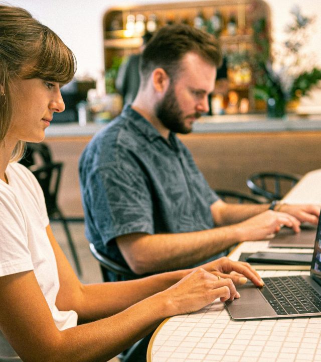 Two young professionals working on laptops in a modern cafe setting.